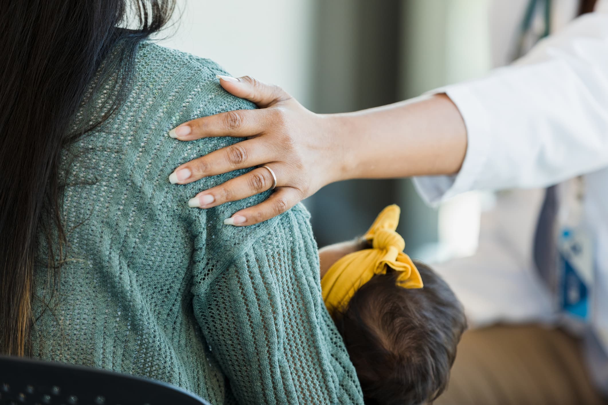 A new mother holding her baby while a clinician rests a hand on her shoulder