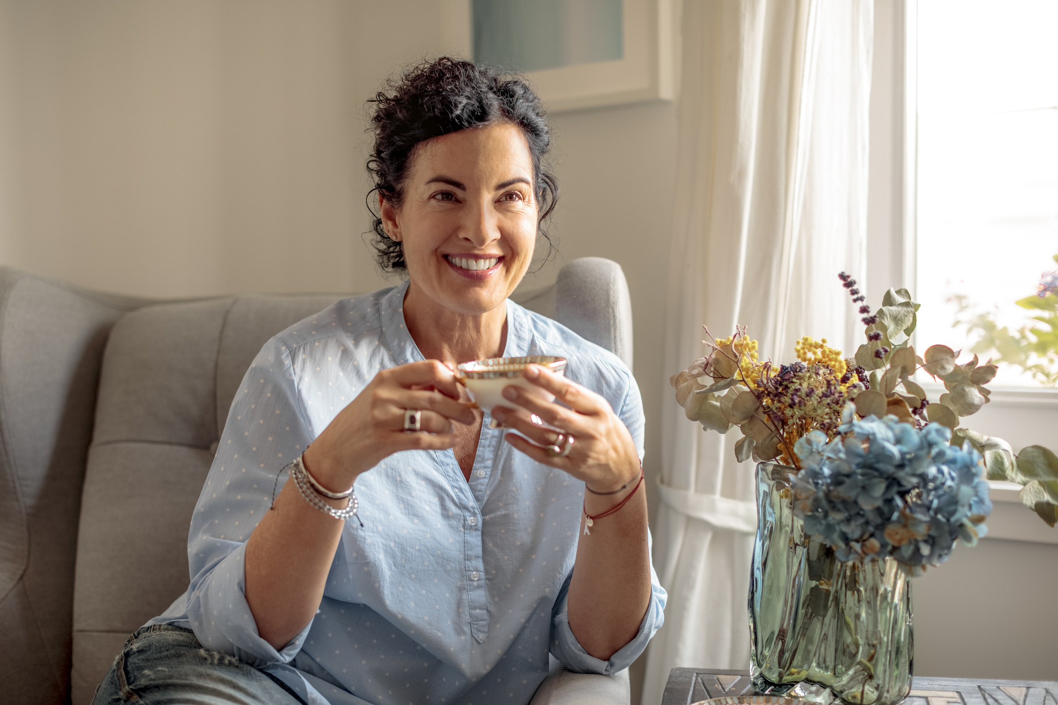 A woman in midlife sitting with a cup of tea in a bright room